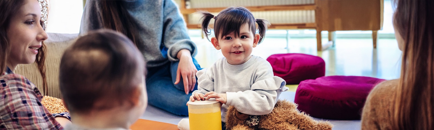Kind spielt mit Baby und haelt einen Gegenstand gelb in der Hand